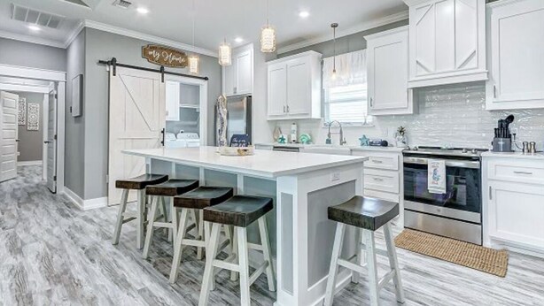 Una cocina moderna con armarios blancos, una isla central con taburetes de bar, iluminación colgante y un horno de acero inoxidable.