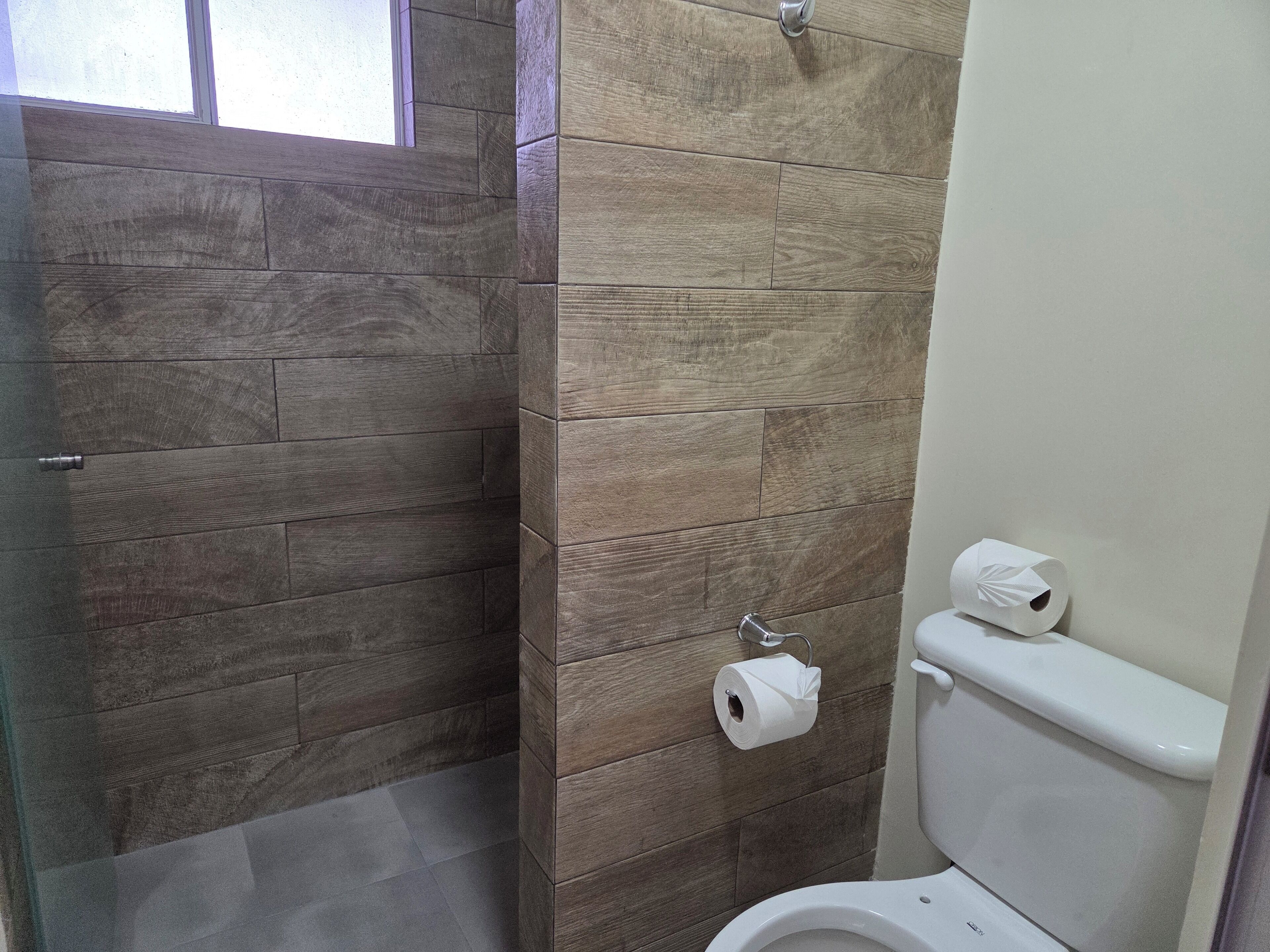 A bathroom with a wooden wall design, a toilet, and two rolls of toilet paper.