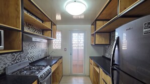 A kitchen with wooden cabinets, a gas stove, a refrigerator, and patterned tiles on the walls. - Lofts by Verticca Héroes (Tecamac)