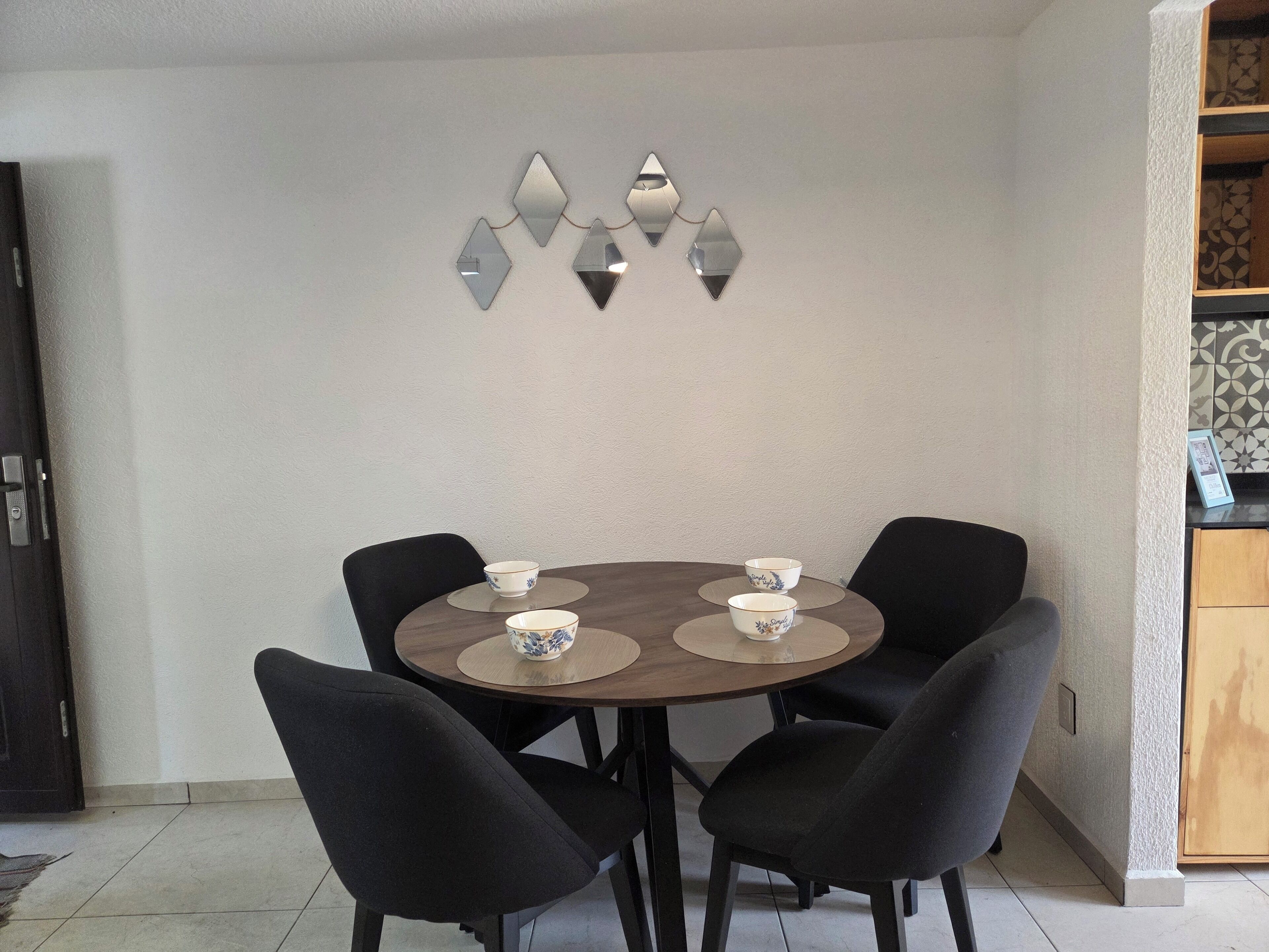 Un comedor con una mesa redonda, cuatro sillas y dos cuencos sobre individuales.