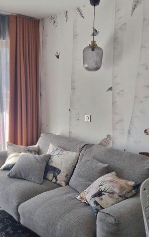 Ein Wohnzimmer mit grauem Sofa, gemusterten Kissen und einer Pendelleuchte.