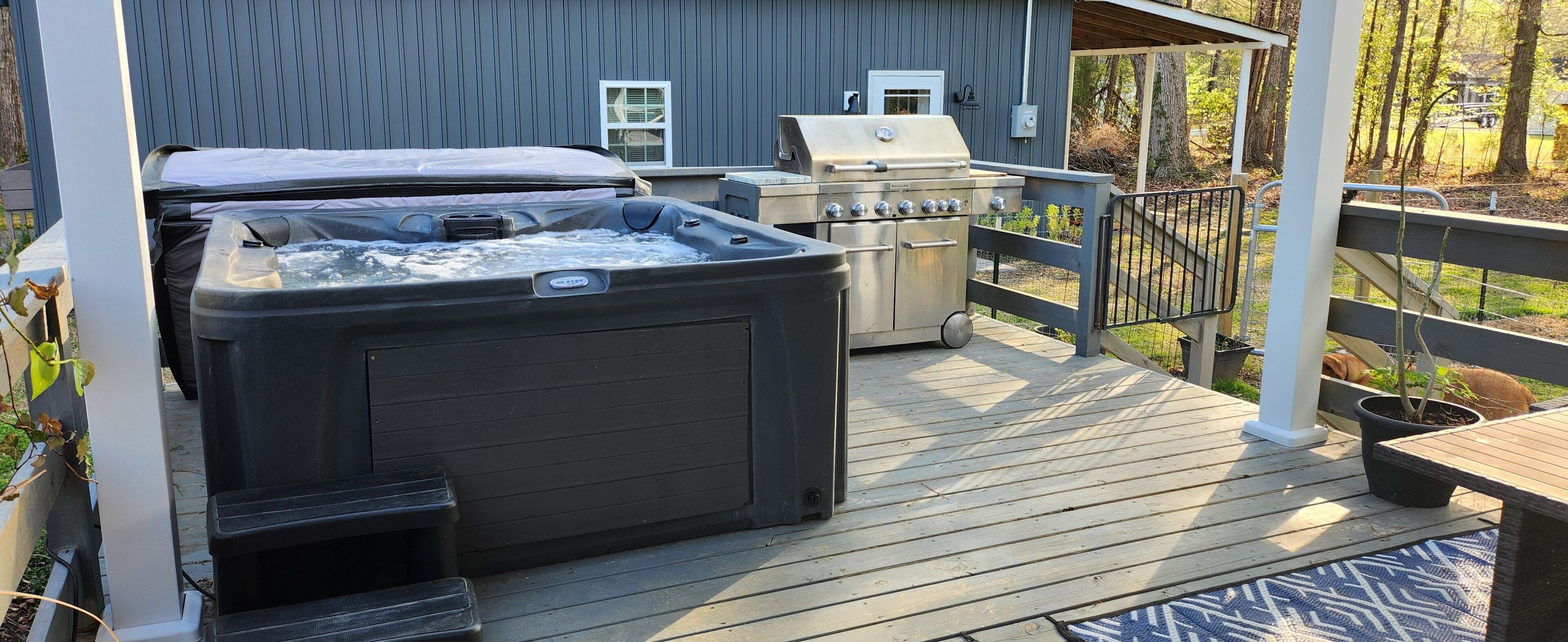 A hot tub, grill, and steps on a wooden deck.