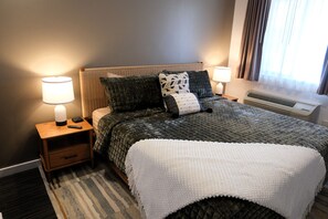 Ein Hotelzimmer mit einem Bett, zwei Nachttischen mit Lampen, einem Heizkörper und einem Fenster mit Vorhängen.