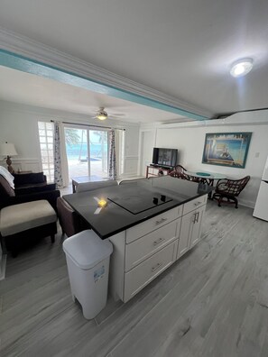A modern kitchen with a central island, white cabinetry, and a dining area with a table and chairs. - Snuggle Beach  Romantic & Charming 1-bedroom Apt. in enchanting East End with AC (East End)