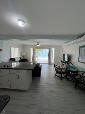 A spacious kitchen with a large island, a dining area with wooden chairs, and a view of the ocean through a glass door. - Snuggle Beach  Romantic & Charming 1-bedroom Apt. in enchanting East End with AC (East End)