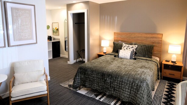A modern hotel room with a large bed, two bedside tables with lamps, a chair, a desk, and a walk-in closet. - Jackrabbit 133 Downtown Moab Studio | Near Arches National Park | Walk to Shops & Dining (Moab)