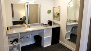 A modern bathroom with a large mirror, a sink, and a coffee maker. There are shelves with toiletries and a trash bin. - Jackrabbit 133 Downtown Moab Studio | Near Arches National Park | Walk to Shops & Dining (Moab)