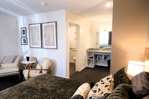A hotel room with a bed, a seating area with chairs, a small table with a plant, and a bathroom visible through an open door. - Jackrabbit 133 Downtown Moab Studio | Near Arches National Park | Walk to Shops & Dining (Moab)