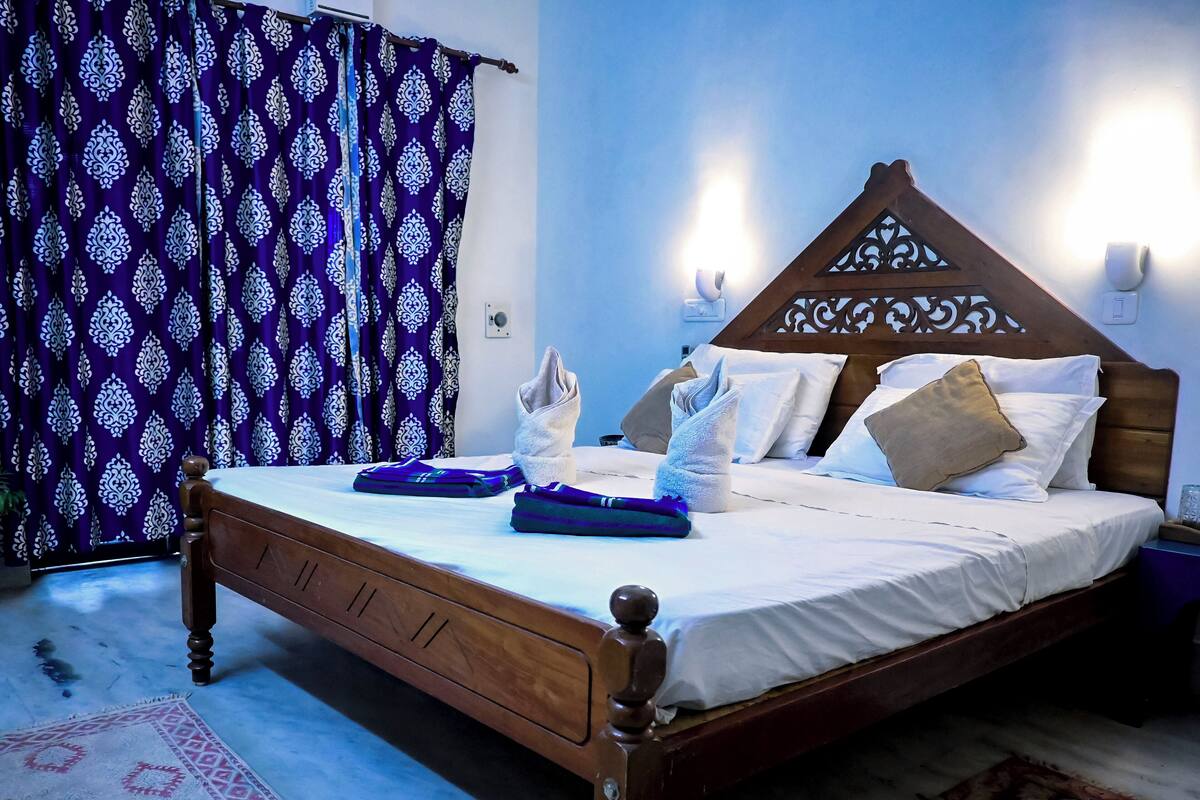 Ein ordentlich bezogenes Bett mit gefalteten Handtüchern, einem gemusterten Teppich und einem blau-weißen Vorhang.
