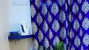 A corner of a room with a blue patterned curtain, a white kettle, a white cup, and a potted plant. - Home City Homestay & Ayurvedic Clinic  (Kovalam)