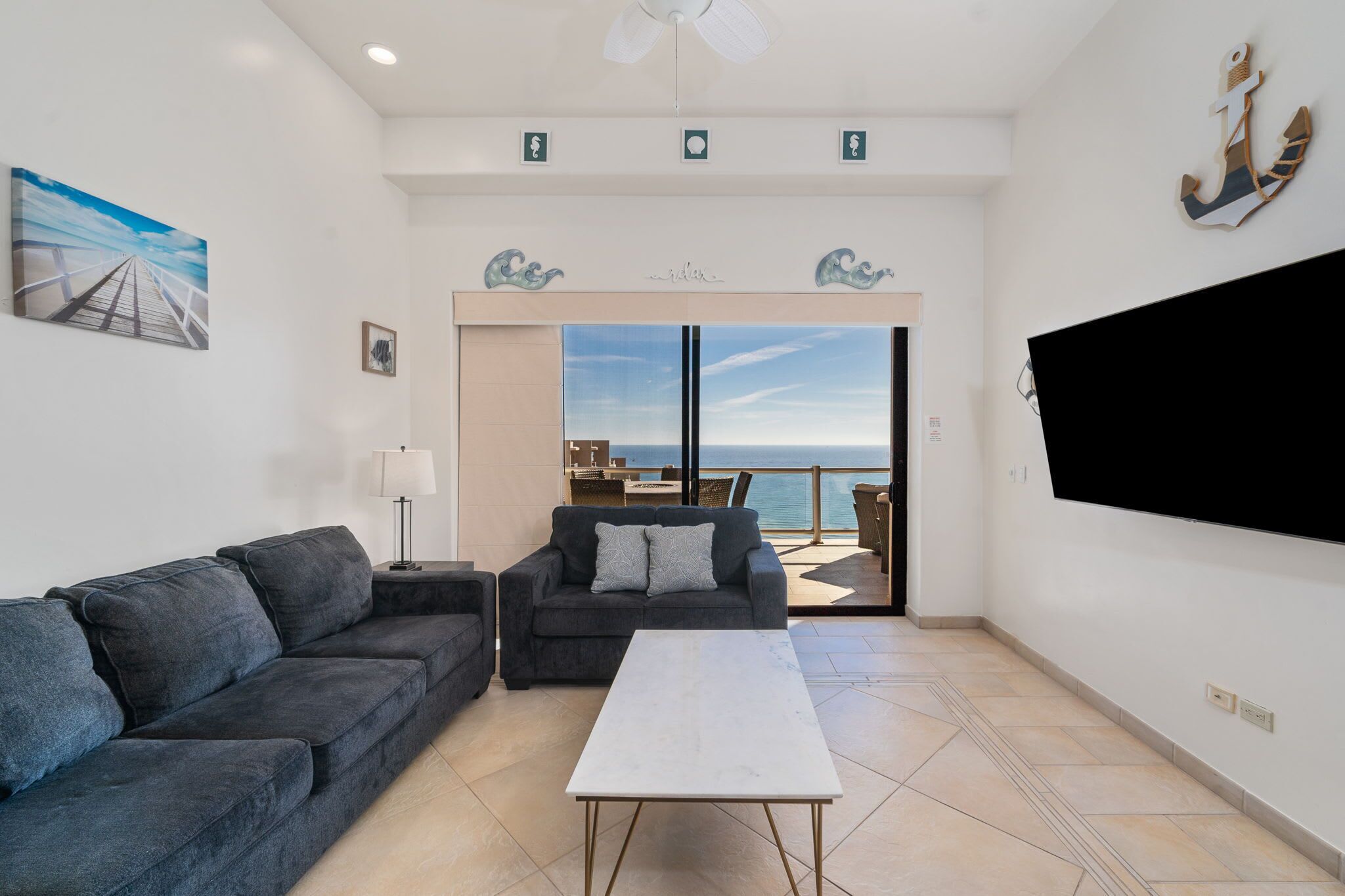 Una sala de estar con sofá, mesa de centro y televisor. Balcón con vista al mar.