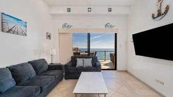 Una sala de estar con sofá, mesa de centro y televisor. Balcón con vista al mar.