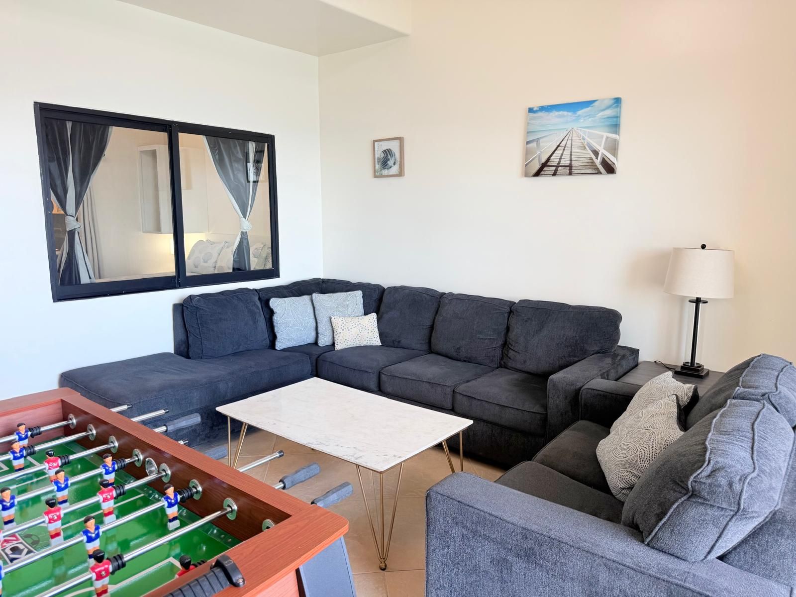 A living room with a sofa, a foosball table, a lamp, and a painting on the wall.