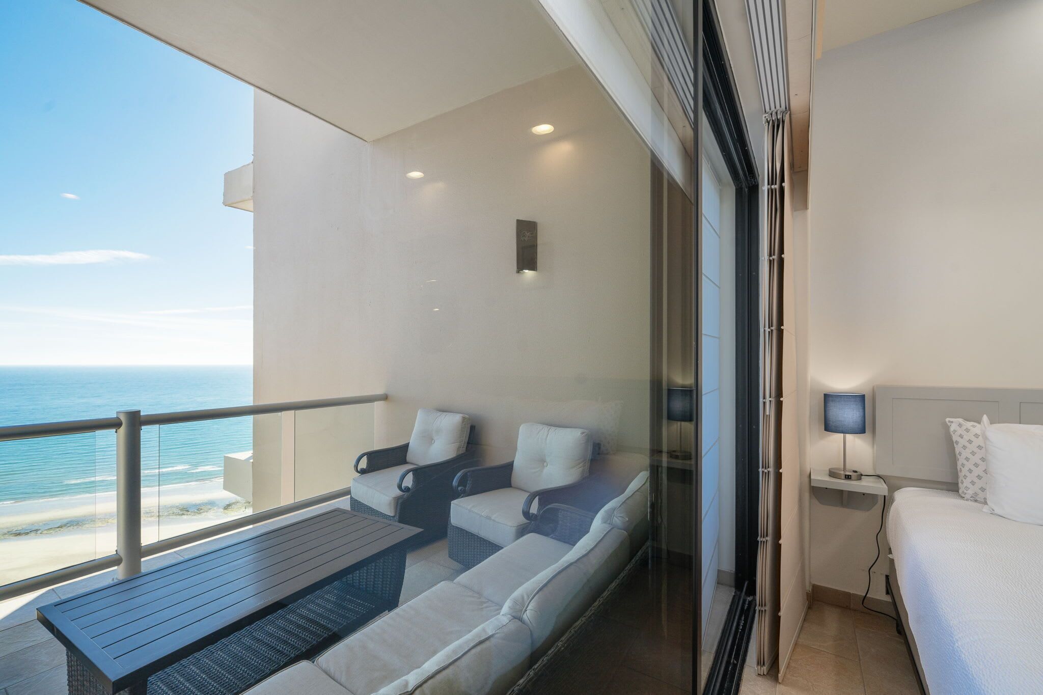 Un balcon avec vue sur l’océan, un lit et une table de chevet avec une lampe.