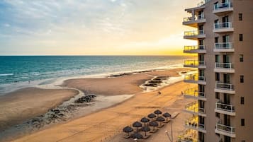 A beachfront hotel with a view of the ocean, a sandy beach, and a row of umbrellas.