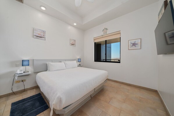 A bedroom with a bed, bedside tables, a nightstand, a window, and artwork on the walls. - Las Palomas 2BR 2BA Ocean View Penthouse (Puerto Peñasco)