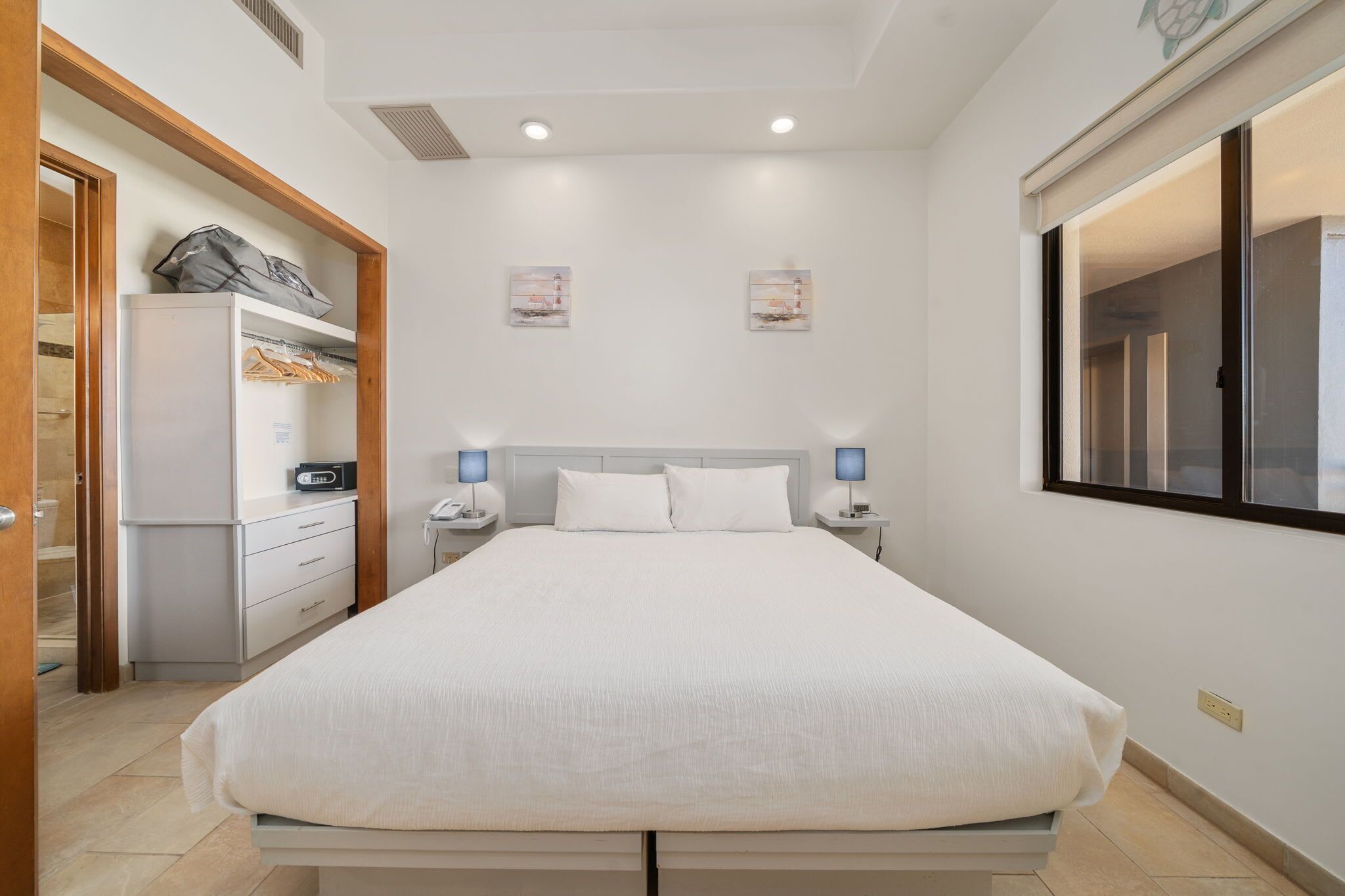 Une chambre à coucher bien rangée, avec un grand lit, des tables de chevet avec des lampes, une armoire et une fenêtre équipée de stores.