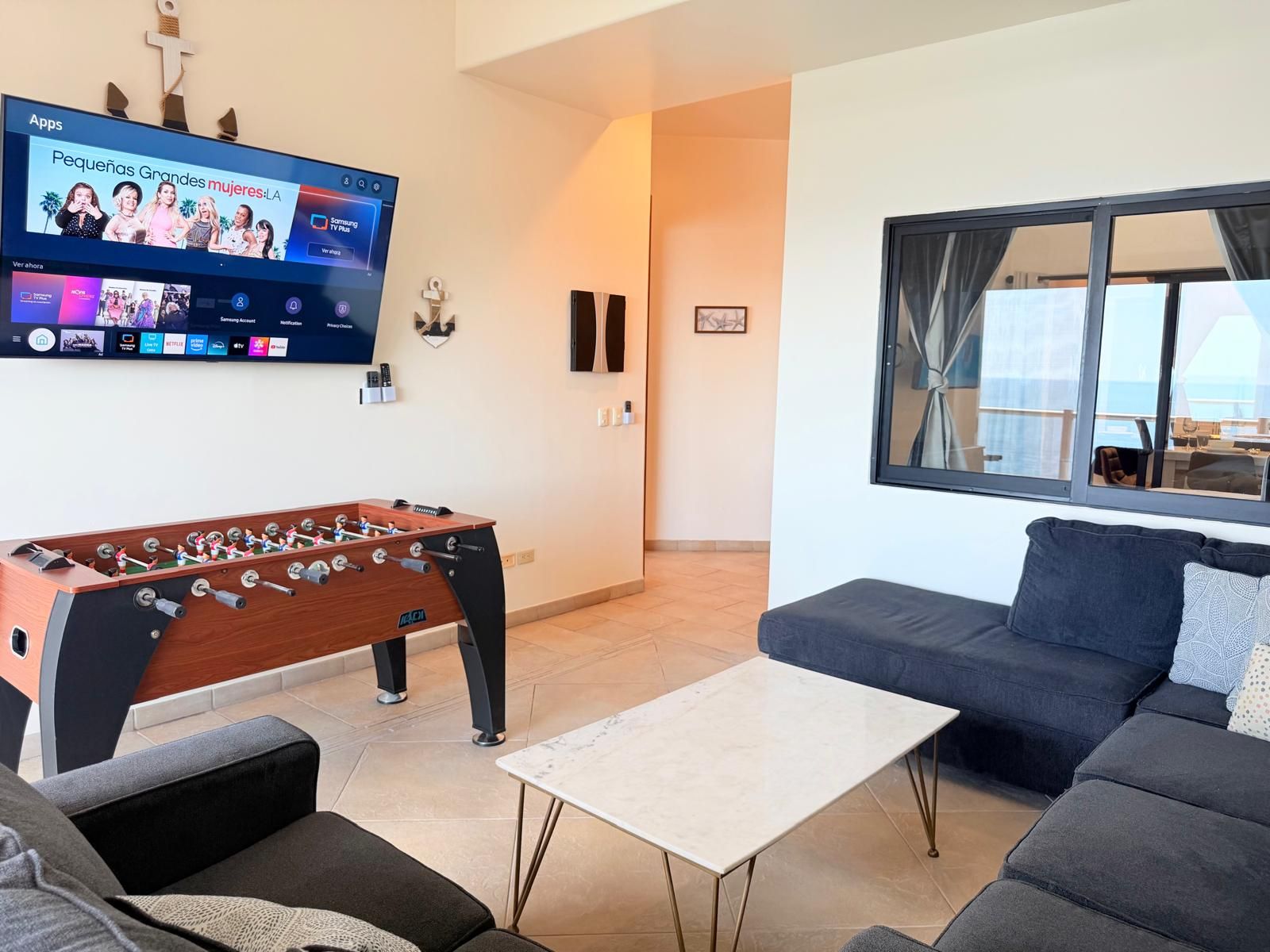 En stue med et bordtennisbord, et fladskærms-tv, en sofa og et vindue med udsigt.
