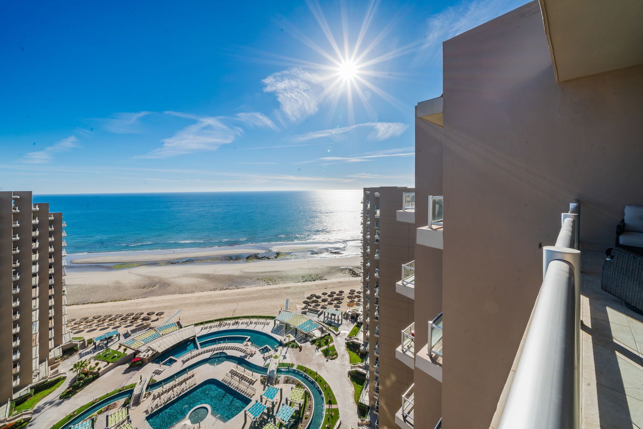 Um hotel com muitos andares com vista para uma praia, área de piscina e espreguiçadeiras.