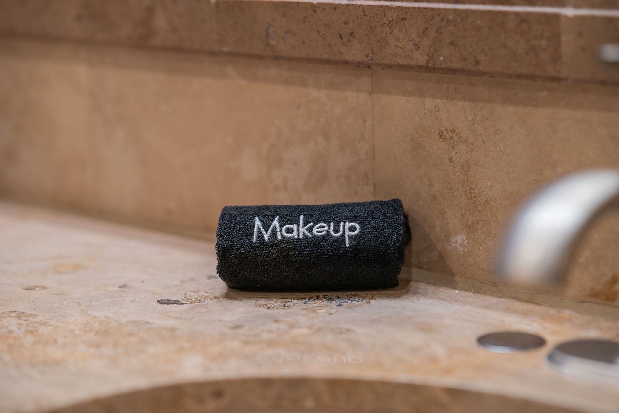 A black towel with the word "Makeup" embroidered on it, placed on a bathroom counter.