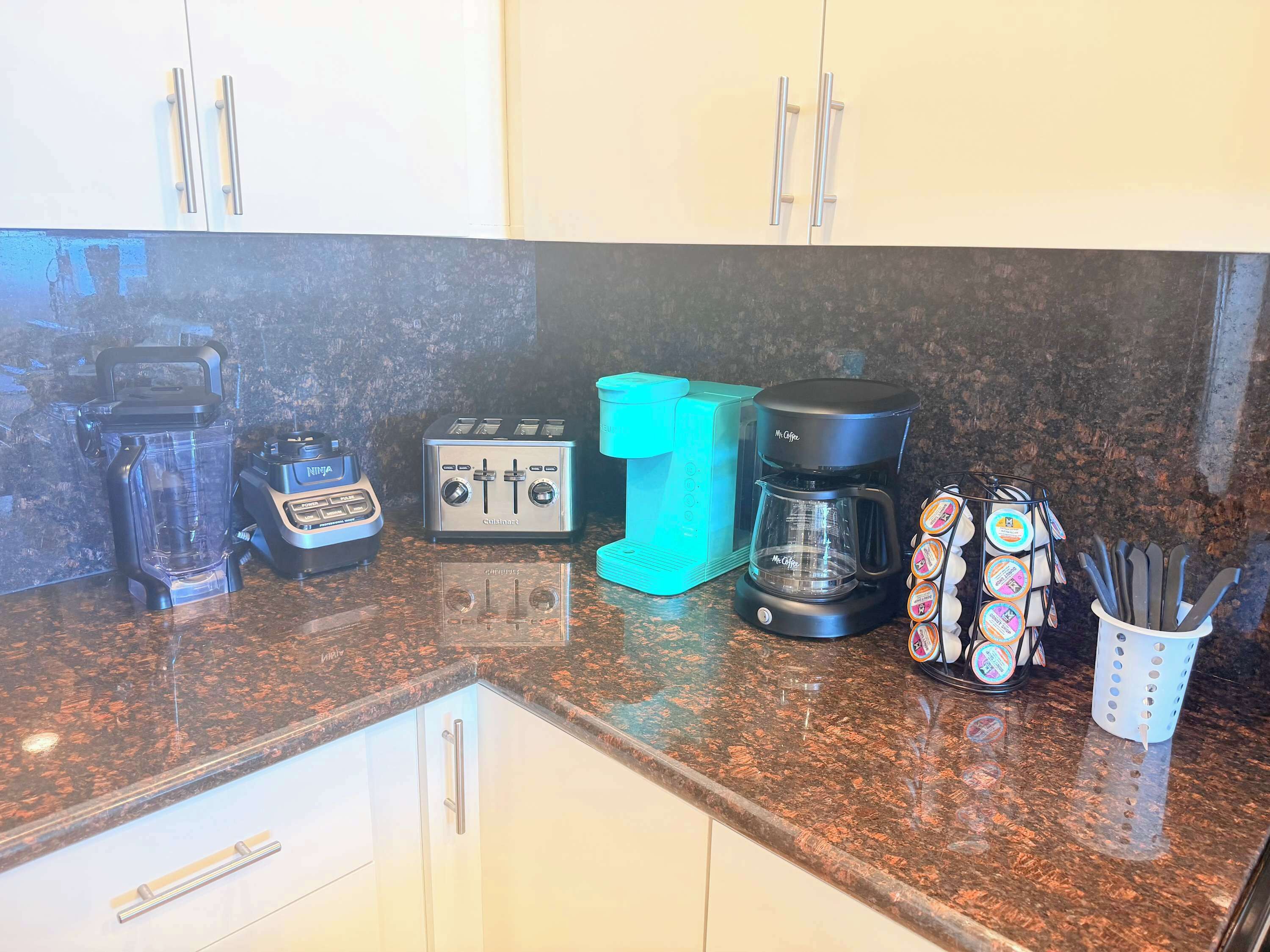 Una cocina con encimera de granito, licuadora, tostadora, cafetera y un portavasos para cuchillos.