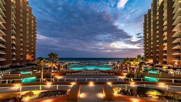 Een resort met een zwembad, palmbomen en uitzicht op de oceaan.