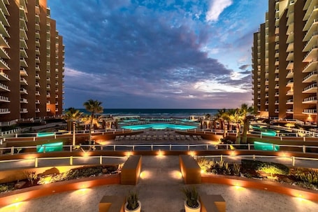 A resort with a pool area, palm trees, and a view of the ocean.