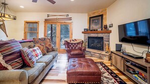 A living room with a fireplace, a television, and a leather ottoman. - Black Bear 50 - Ski-In/Out Durango Townhome (Durango)