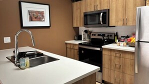 A modern kitchen with wooden cabinets, a stainless steel sink, a microwave, and a refrigerator. - Cozy Home in Lake Country (Kelowna)