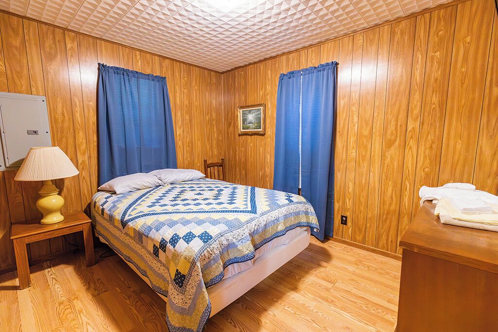 A wooden-paneled room with a bed, a nightstand with a lamp, and a small table with towels.