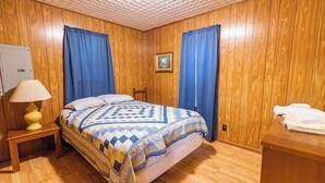 Ein Zimmer mit Holzwänden, einem Bett, einem Nachttisch mit Lampe und einem kleinen Tisch mit Handtüchern.