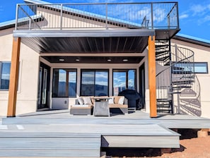 En moderne udendørs terrasse med indbygget siddeområde, en spiraltrappe og store vinduer med udsigt over det omkringliggende landskab.