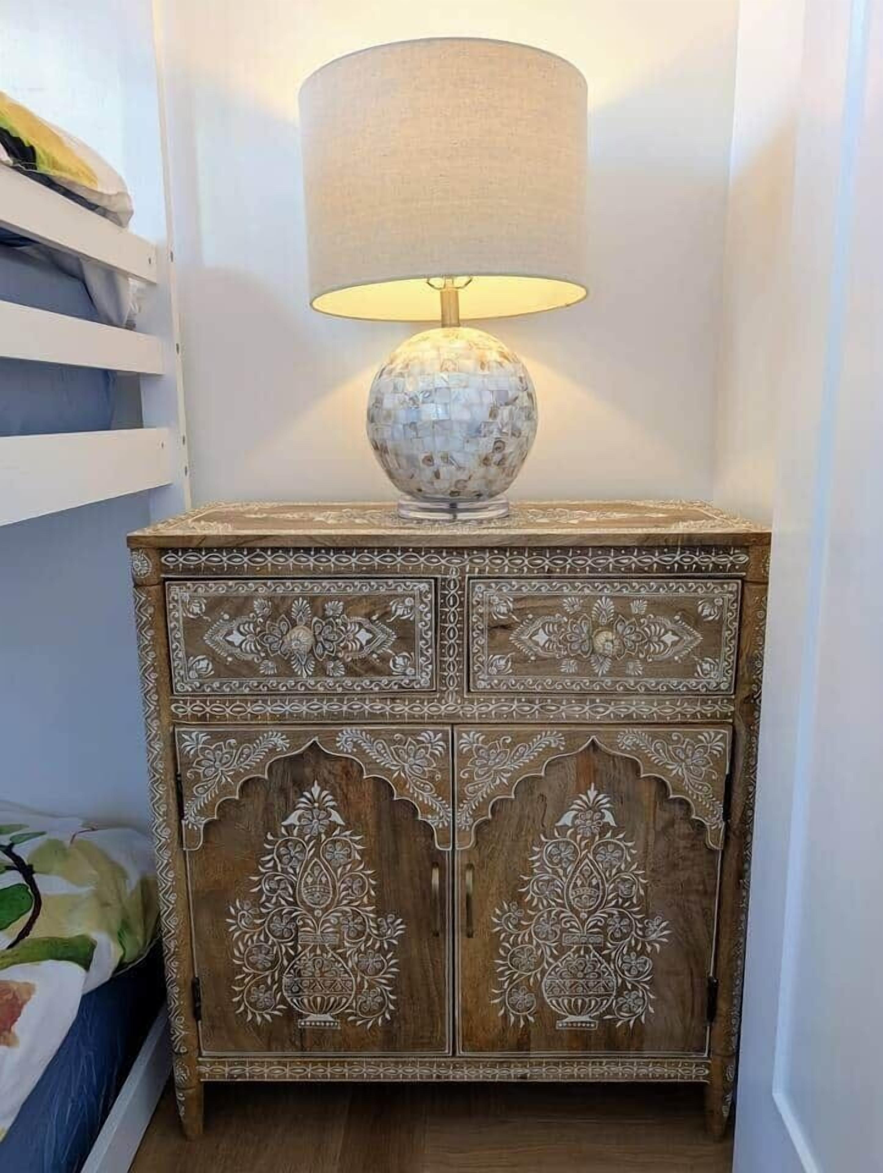 A wooden nightstand with intricate carvings and a lamp on top.