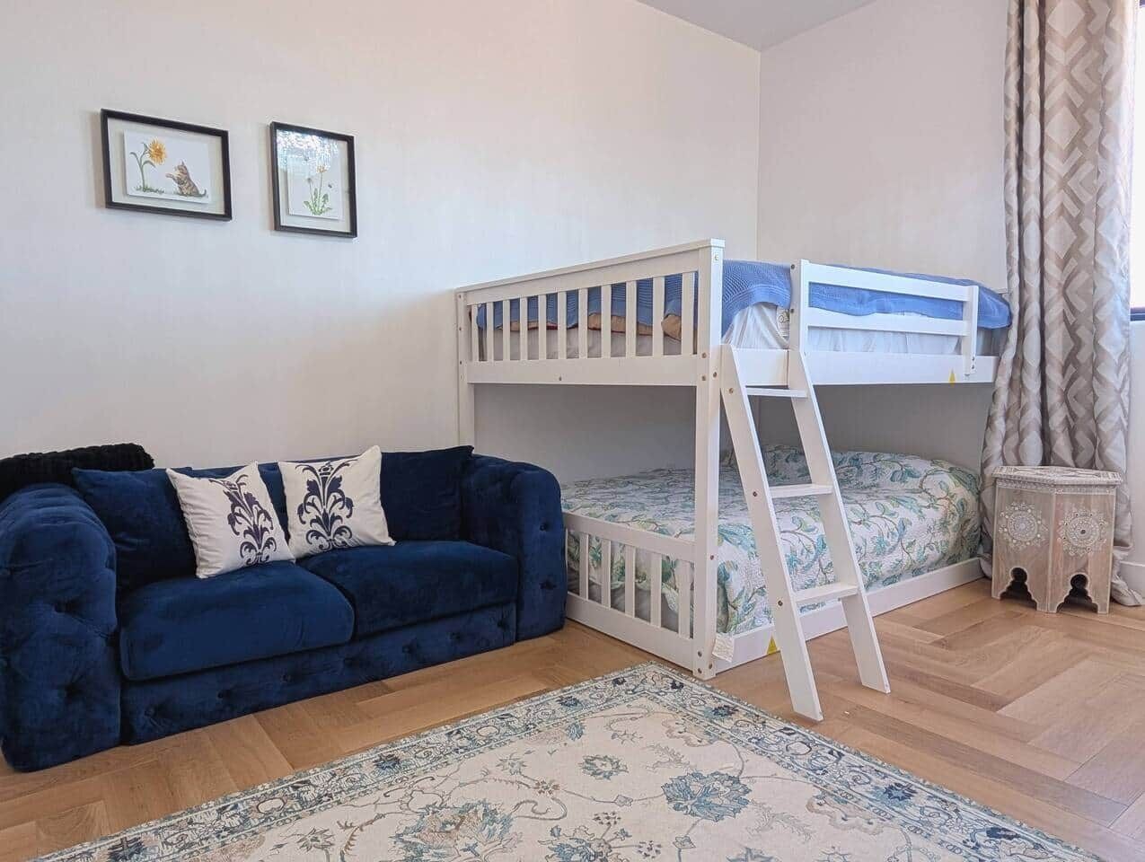 A room with a bunk bed, a blue sofa, and a patterned rug.