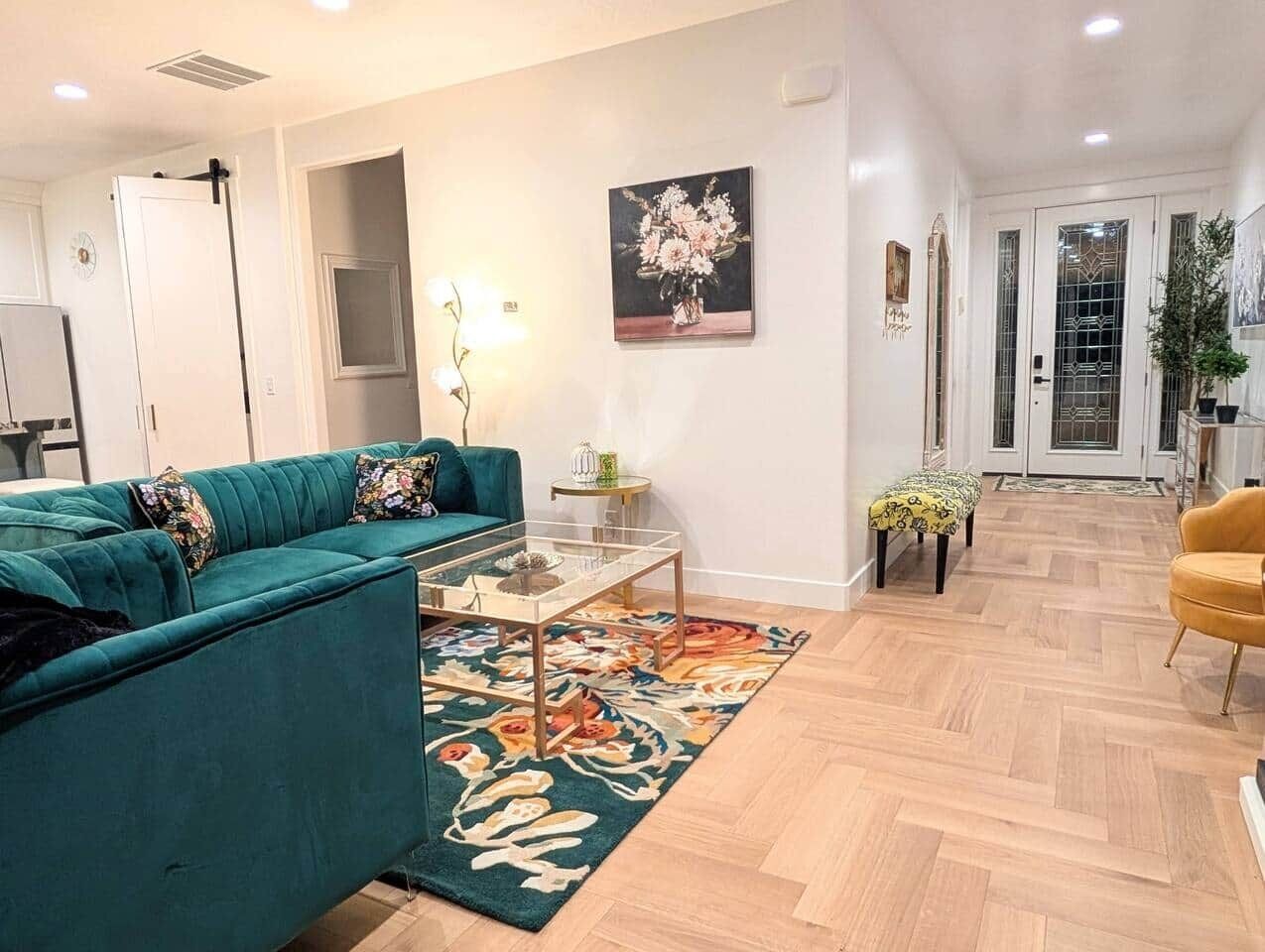 A living room with a teal sofa, a glass coffee table, and a patterned rug.