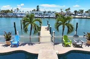 A waterfront view with a dock, palm trees, and a pool area with chairs. -  Treasure Island condo with pool and jacuzzi (Treasure Island)