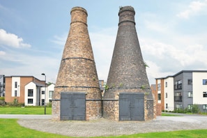 Two brick chimneys with doors, surrounded by modern buildings. - 3BDR Kiln Side | Private Parking | Garden (Stoke-on-Trent)