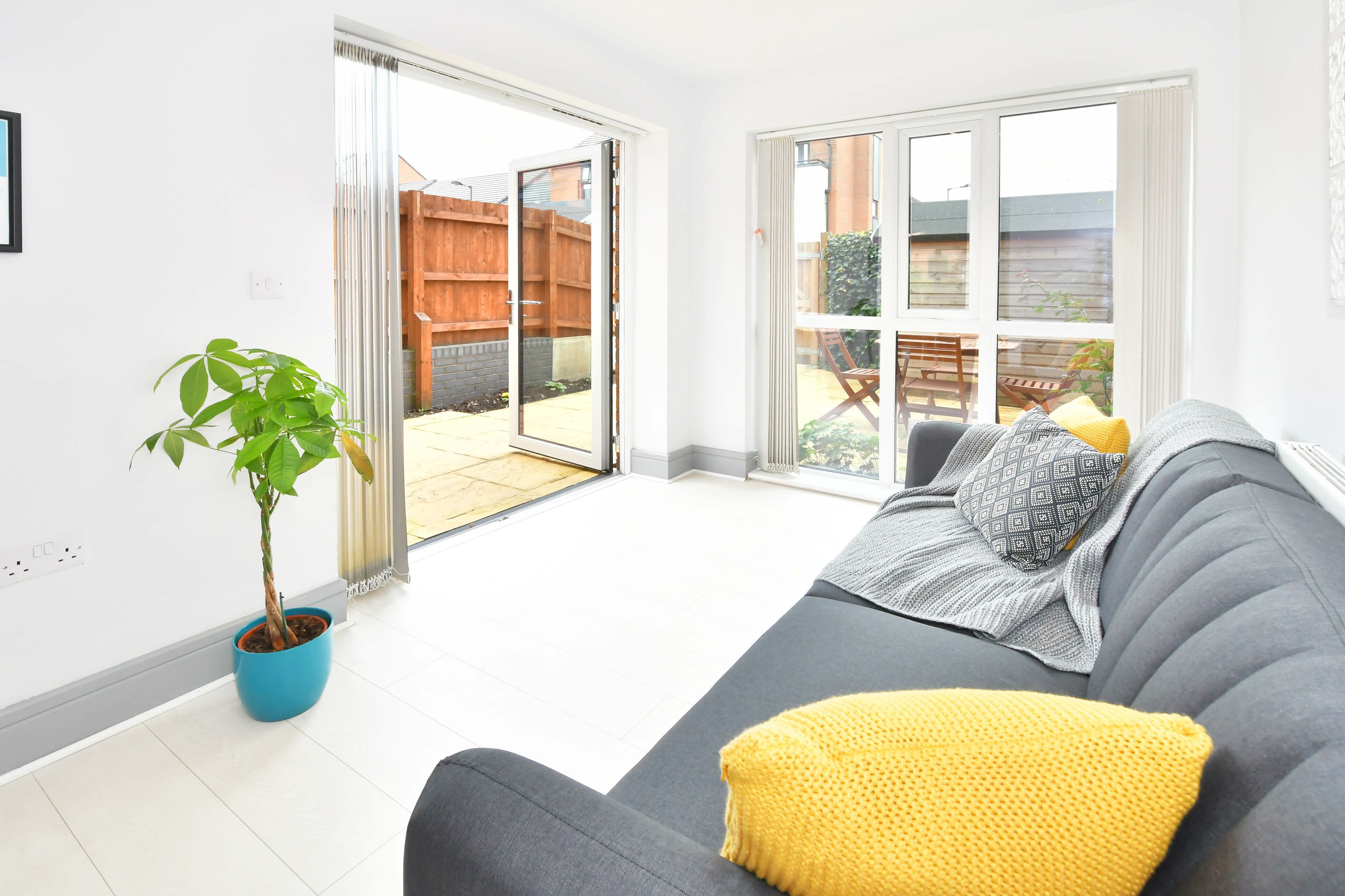 A modern living room with a grey sofa, a yellow throw pillow, a blue potted plant, and a sliding glass door leading to an outdoor area.