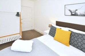 A hotel room with a bed, a bedside table, a lamp, a framed picture on the wall, and a coat rack. - 3BDR Kiln Side | Private Parking | Garden (Stoke-on-Trent)