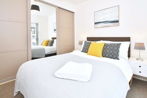 Een hotelkamer met een bed, nachtkastje, lamp, spiegel en een schilderij aan de muur.