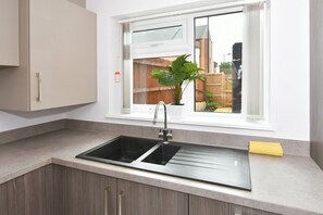Une cuisine équipée d’un évier à deux bacs, d’une fenêtre donnant sur l’extérieur et d’une plante posée sur le rebord de la fenêtre.