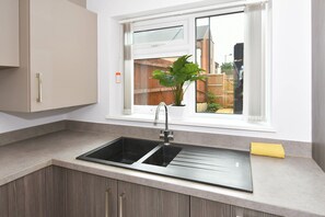 A kitchen with a double sink, a window with a view of the outside, and a plant on the windowsill. - 3BDR Kiln Side | Private Parking | Garden (Stoke-on-Trent)