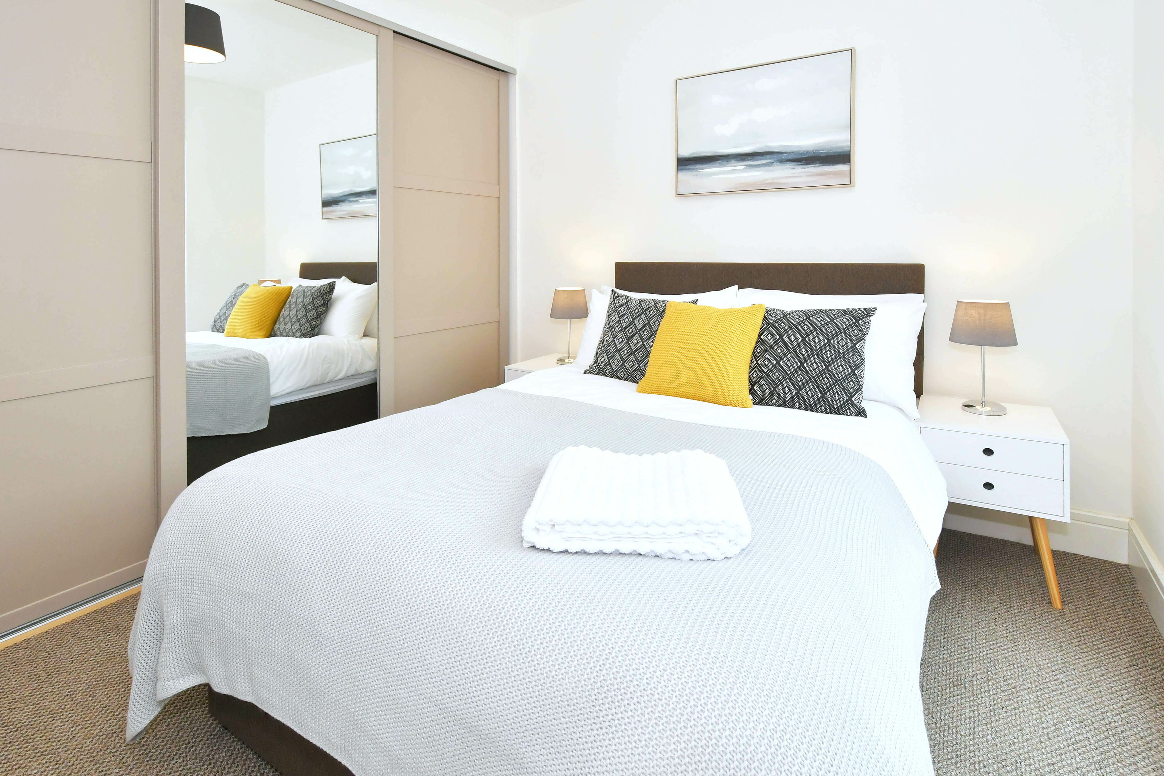 Une chambre d’hôtel avec un lit, une table de chevet, une lampe, un miroir et un tableau au mur.