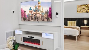 A modern bedroom with a flat-screen TV mounted above a fireplace, a bed with a headboard, and a bedside table with a lamp. - 1BR Family Apt, Minutes to Universal & Epic (Orlando)