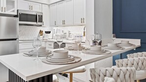 A modern kitchen with white cabinetry, stainless steel appliances, and a central island with dining setup. - 1BR Family Apt, Minutes to Universal & Epic (Orlando)