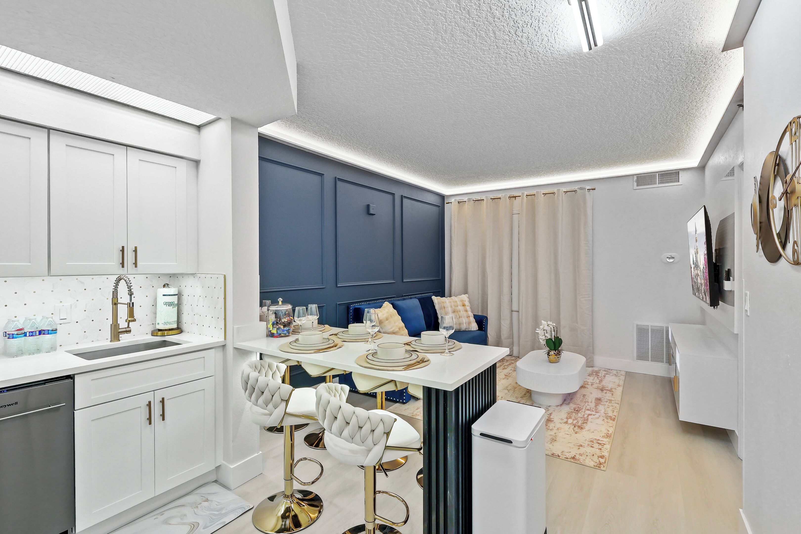 A modern kitchen with white cabinets, a built-in oven, and a dining area with a white table set for four.