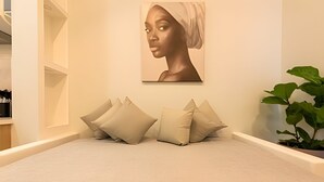 Een slaapkamer met een bed, kussens, een kunstwerk aan de muur en een potplant.