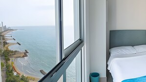 Ein Hotelzimmer in einem Hochhaus mit großem Fenster, Blick auf Strand und Stadt.