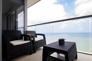Ein Balkon mit zwei Korbstühlen und einem kleinen Tisch, mit Blick auf ein Gewässer.