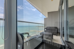 Un balcon doté de meubles en osier, d’une rambarde en verre et offrant une vue sur la mer.